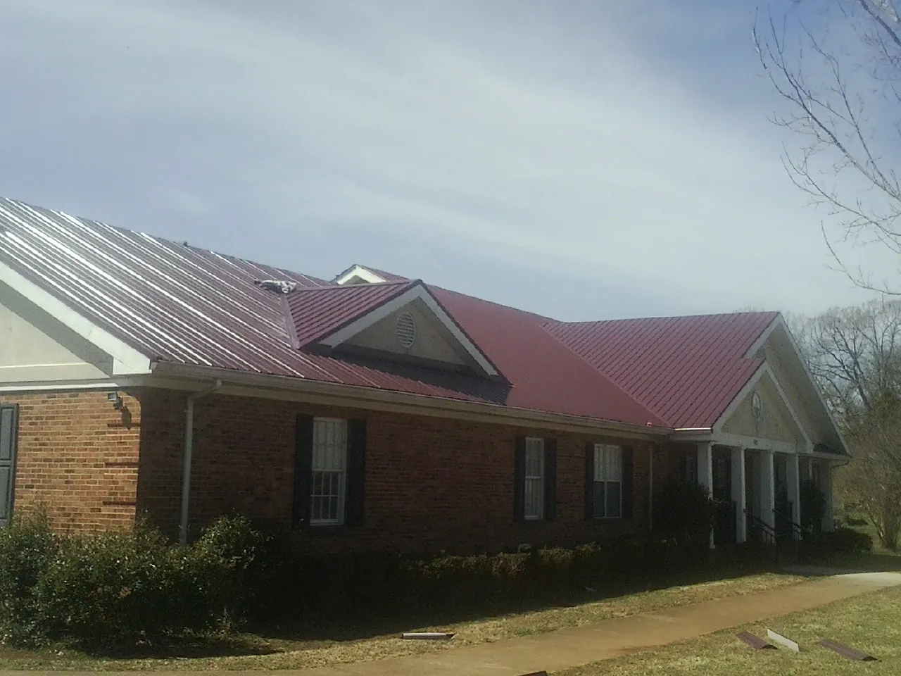 Red metal roof with gabled entries on a long brick building, from a Hail Damage Roof Repair job in Salt Lake City