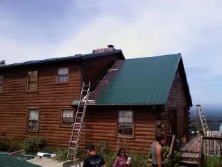 Green metal roof going on a two story log home with ladders set in Salt Lake City