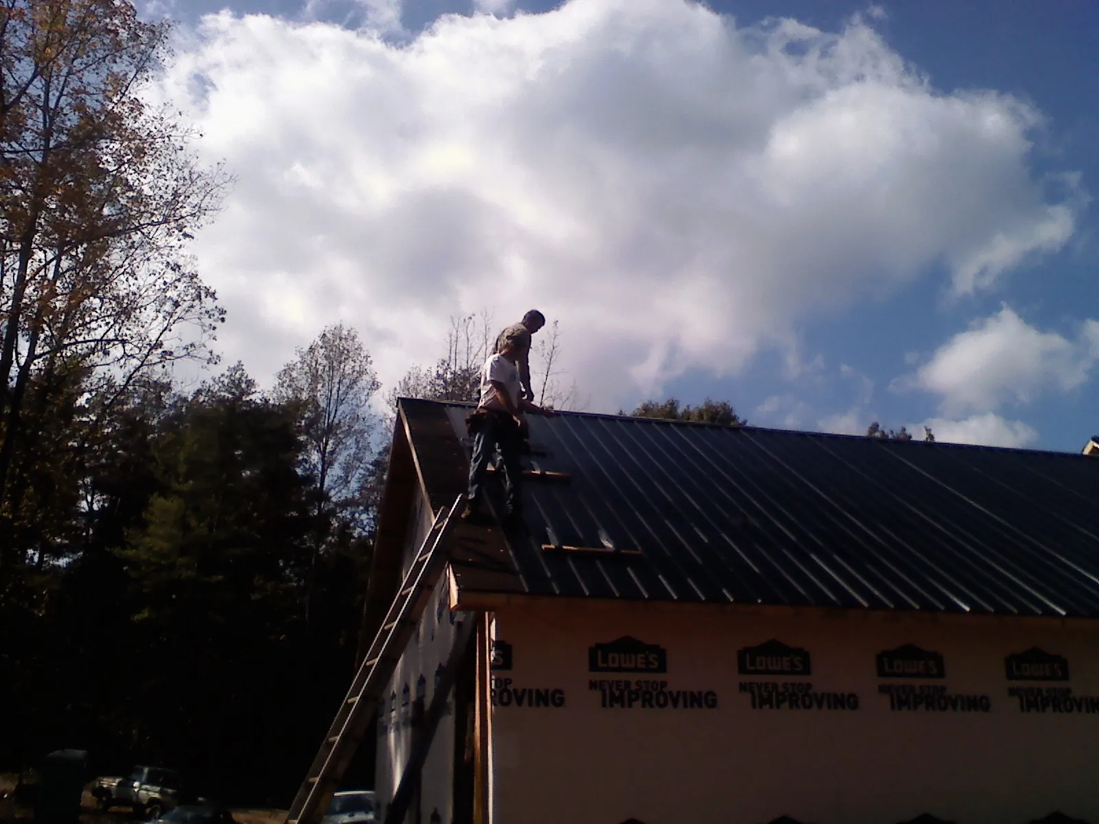 Roofer fastening dark metal panels high against a cloudy sky, from a Roof Inspection job in Salt Lake City