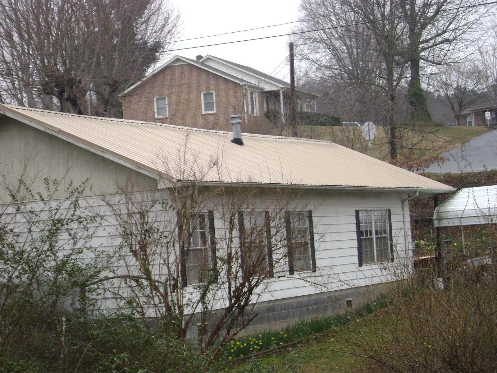 Tan metal roof on a white sided house set into a hillside — Commercial Roofing by Roofing Brothers in Salt Lake City